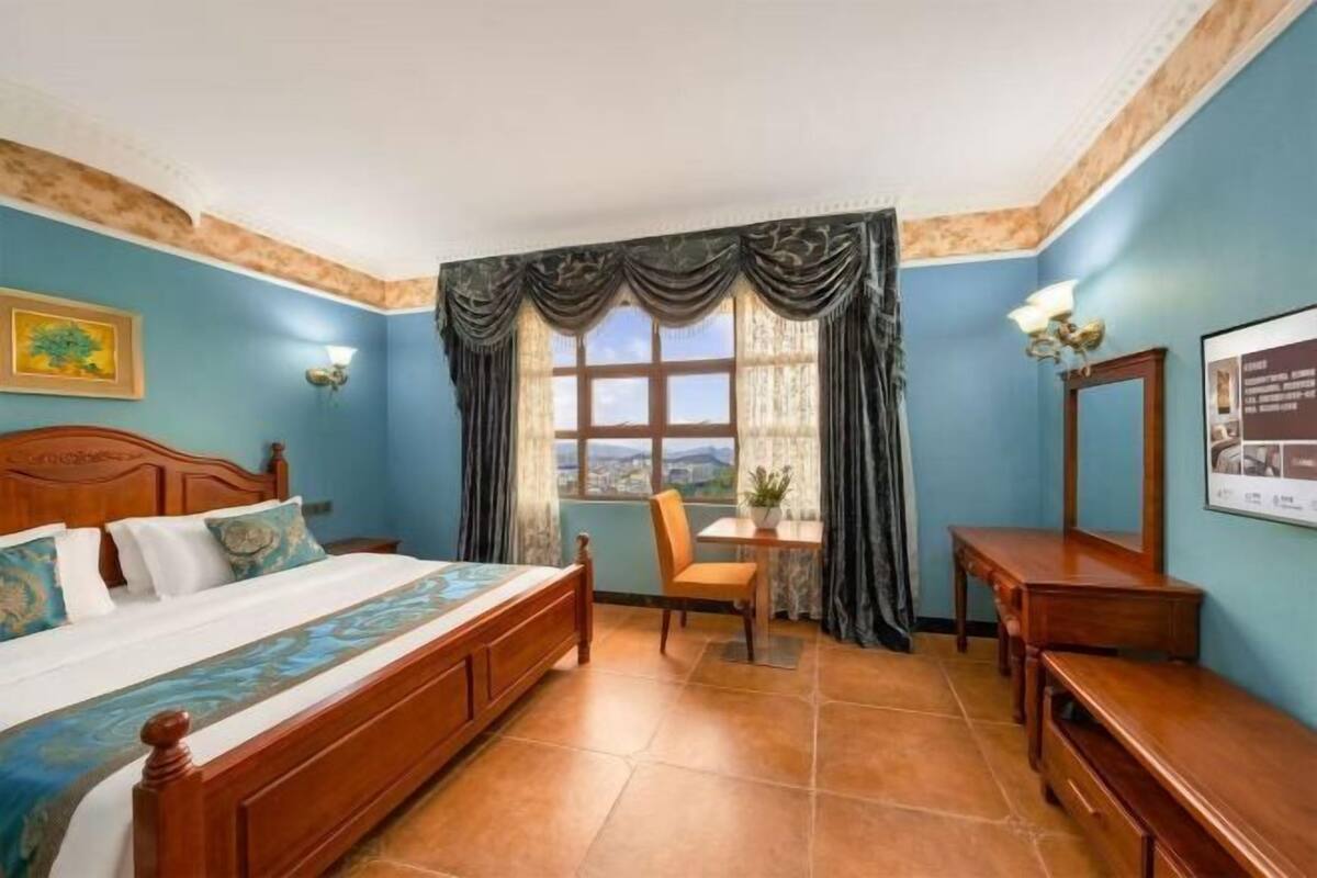 Un dormitorio con cama, escritorio, silla, ventana con cortinas y vistas.