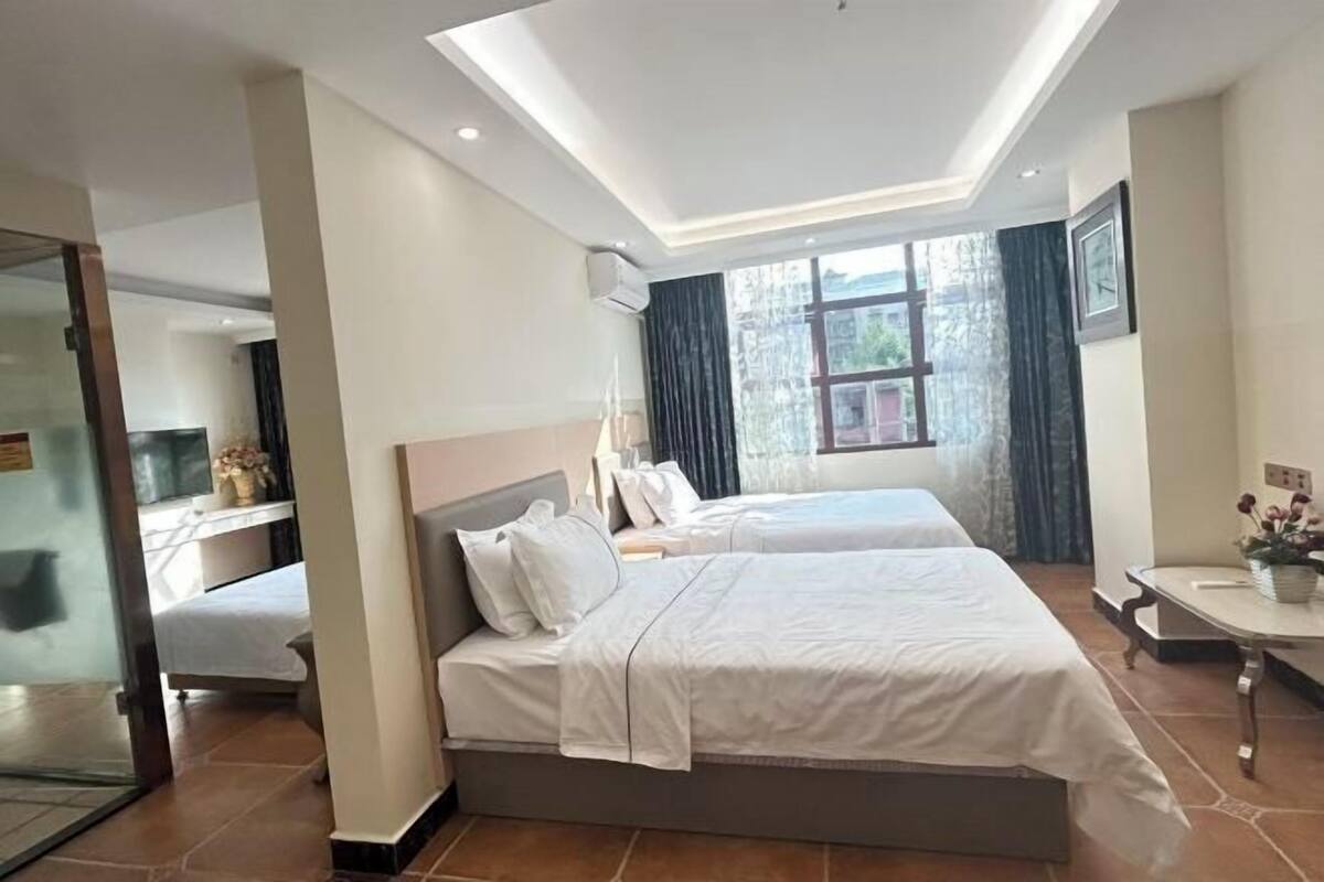Habitación de hotel con dos camas, un escritorio, una silla y un ventanal con cortinas.