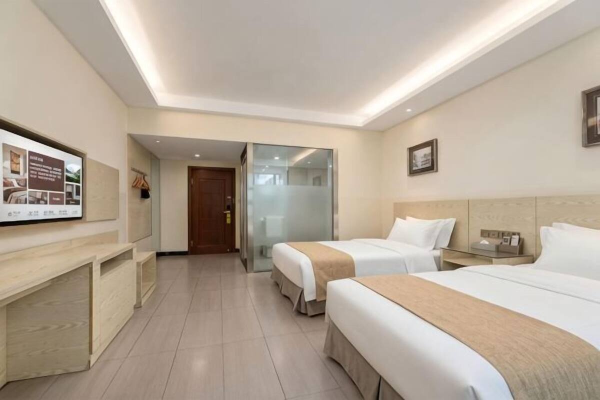 Habitación de hotel con dos camas, un escritorio, un televisor y una puerta que da a otra habitación.