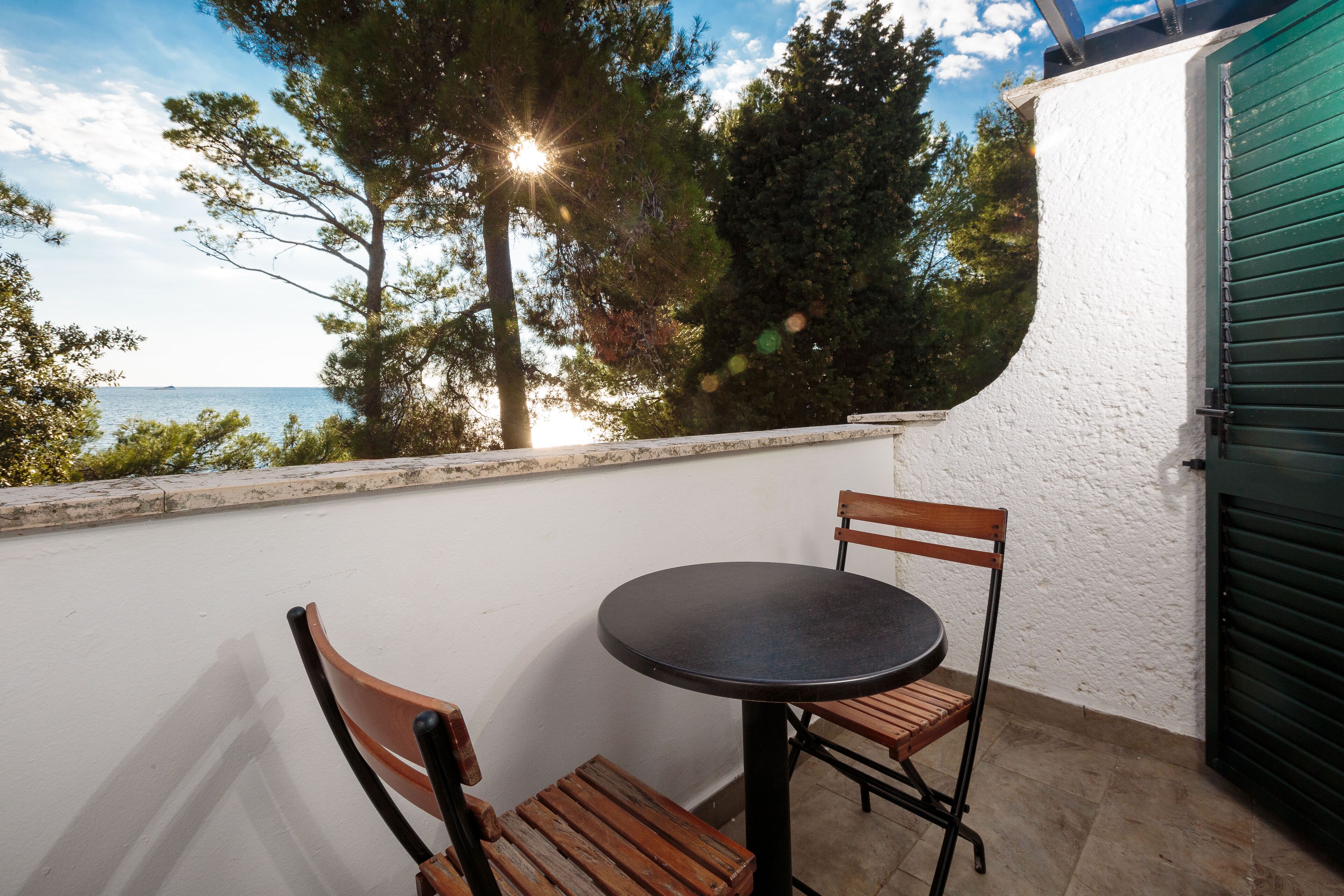 A balcony with a round table and two wooden chairs, overlooking a body of water and trees.
