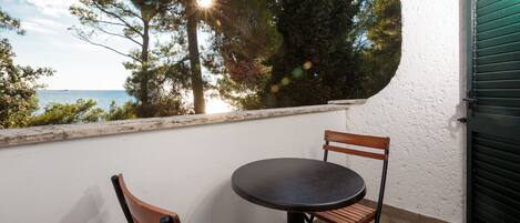 A balcony with a round table and two wooden chairs, overlooking a body of water and trees.