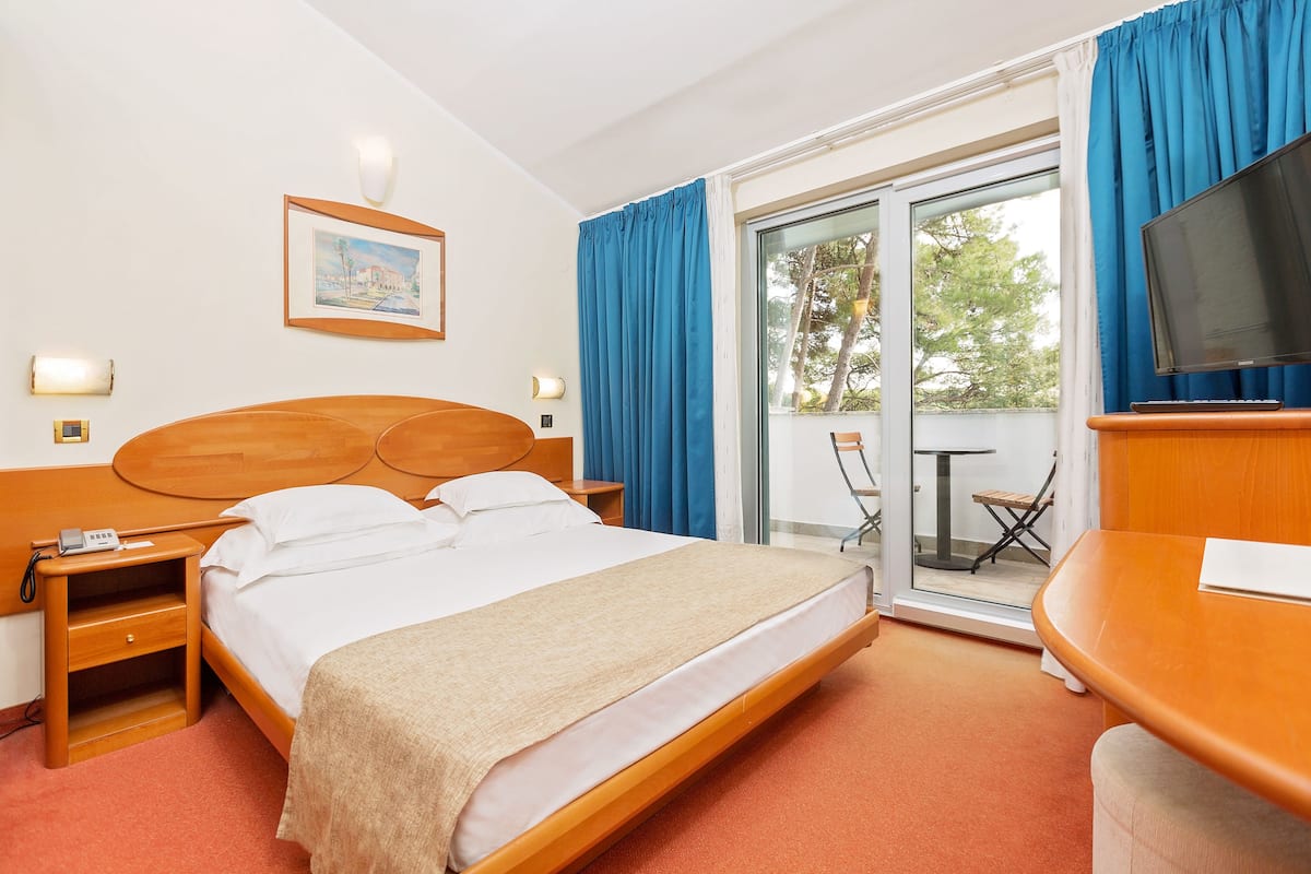 A hotel room with a bed, bedside table, lamp, and a TV.