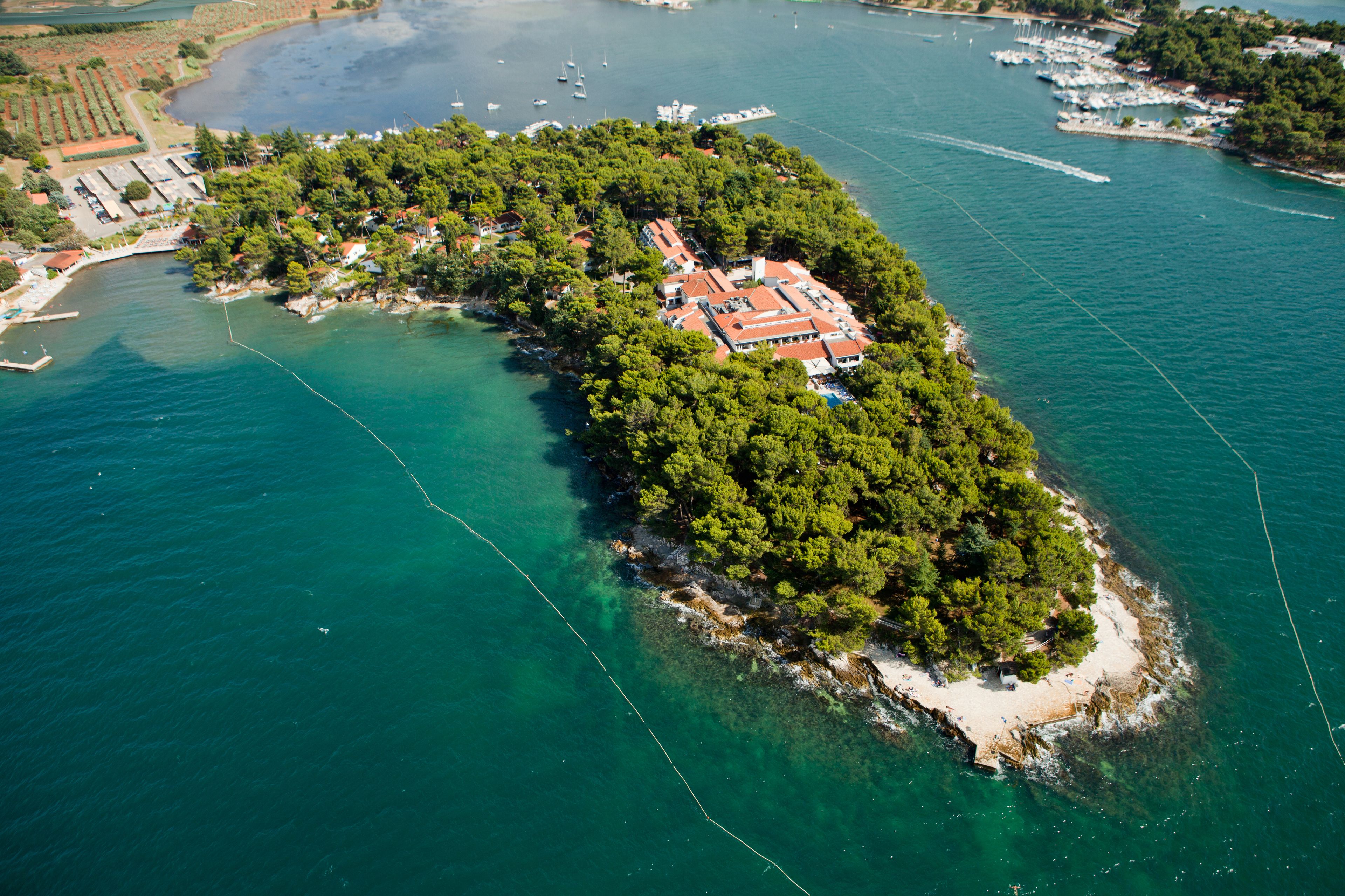 An aerial view of a coastal island with a cluster of buildings, clear turquoise waters, and boats.