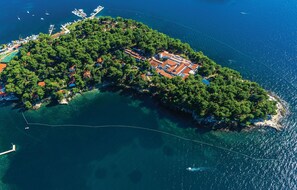 An aerial view of a coastal island with dense greenery, a marina, and buildings with red roofs. - Villa Galijot Plava Laguna (Porec)