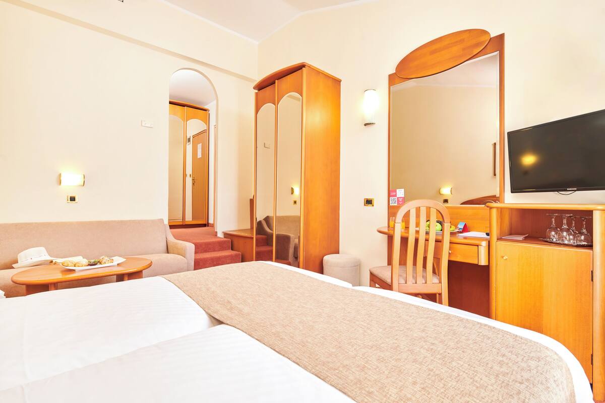 A hotel room with a bed, a desk with a chair, a television, and a small table with a plate of food.