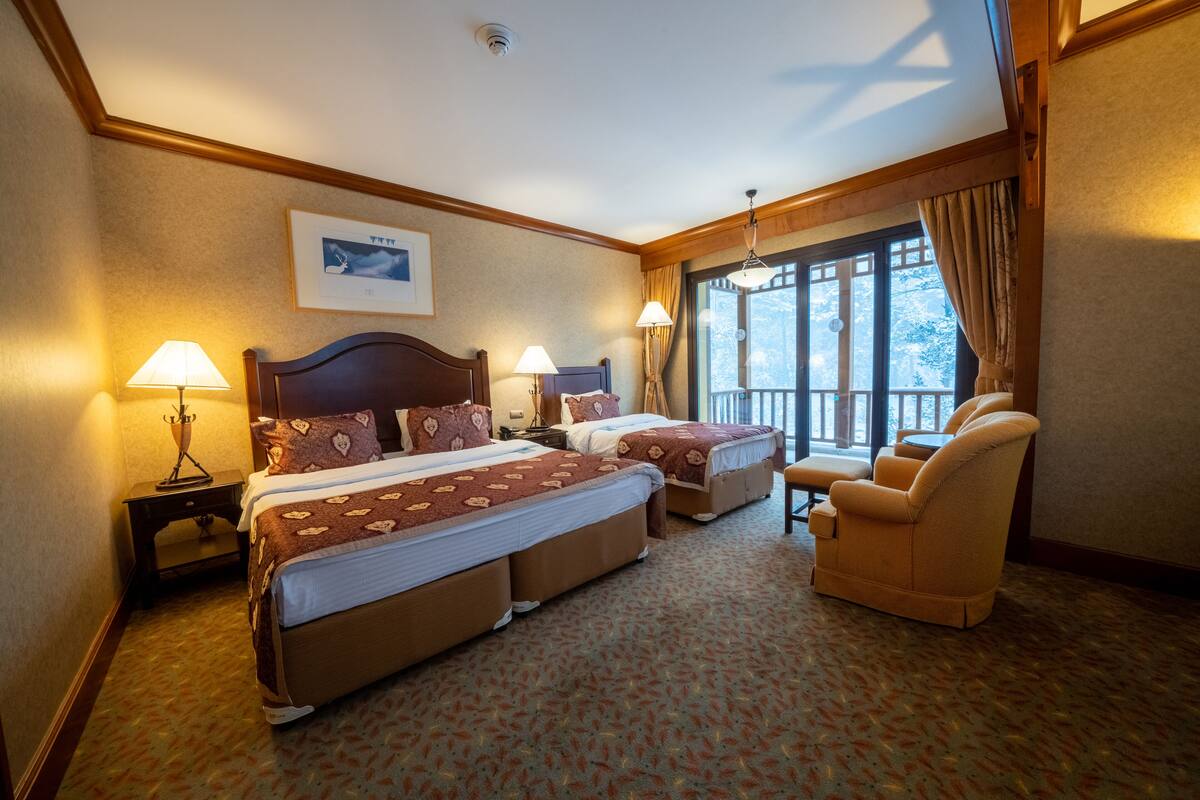 Een hotelkamer met twee bedden, een bank, een stoel en een groot raam met gordijnen.