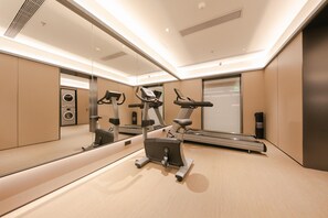 Une salle de sport moderne équipée de machines d’exercice, d’un grand miroir et d’un lave-linge fixé au mur.