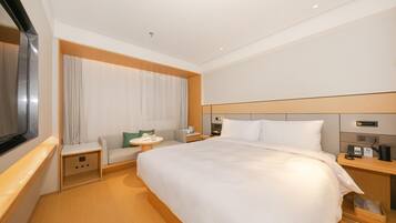 Habitación de hotel con una cama grande, un área de descanso con una mesa, un televisor y una mesita de noche con teléfono y lámpara.
