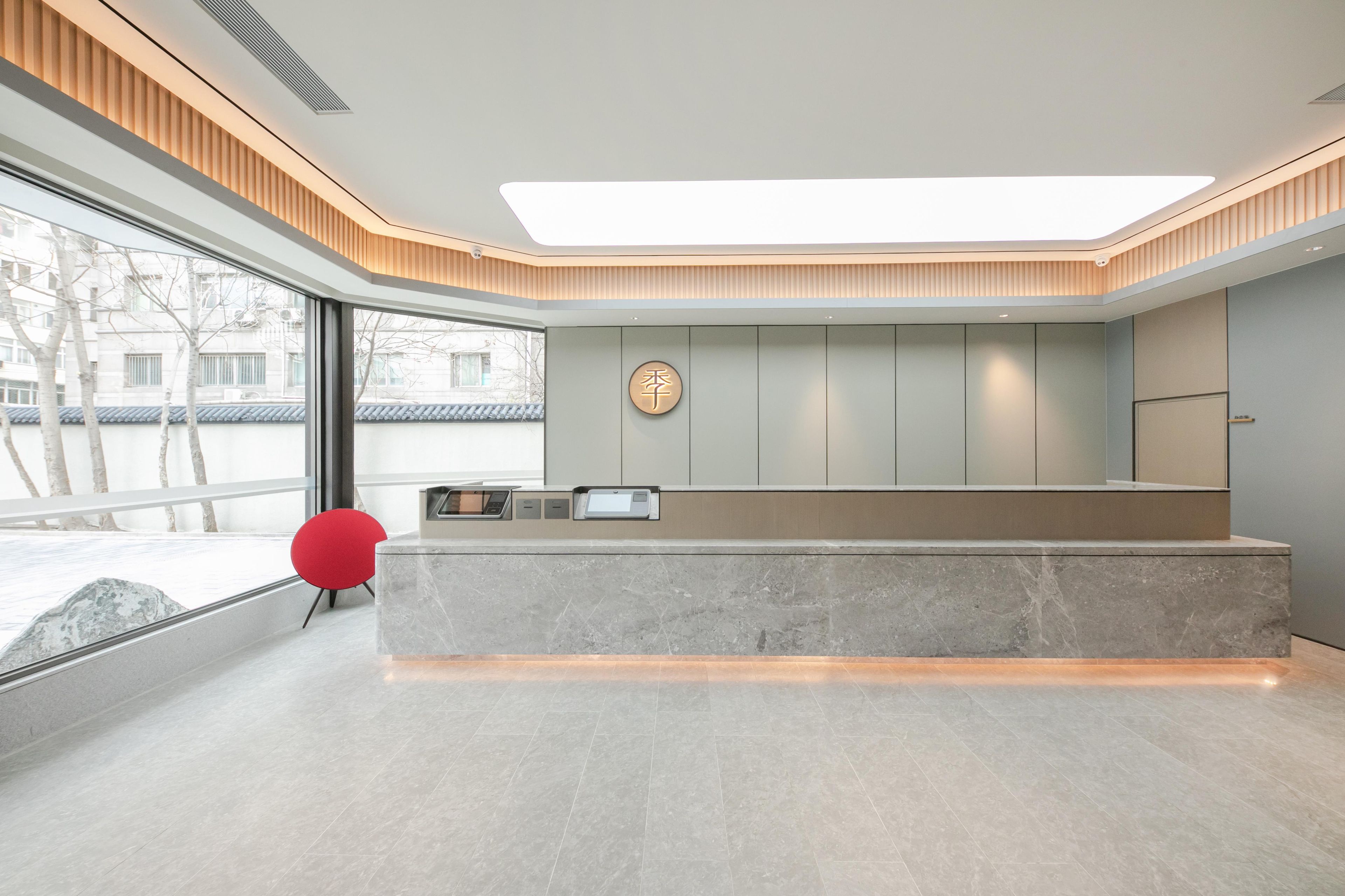 Un espace d’accueil moderne avec un comptoir en marbre, un fauteuil rouge et une grande fenêtre donnant sur l’extérieur.