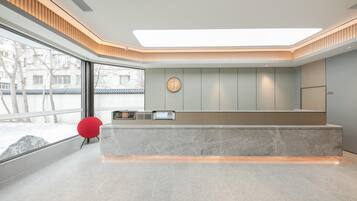 Un espace d’accueil moderne avec un comptoir en marbre, un fauteuil rouge et une grande fenêtre donnant sur l’extérieur.