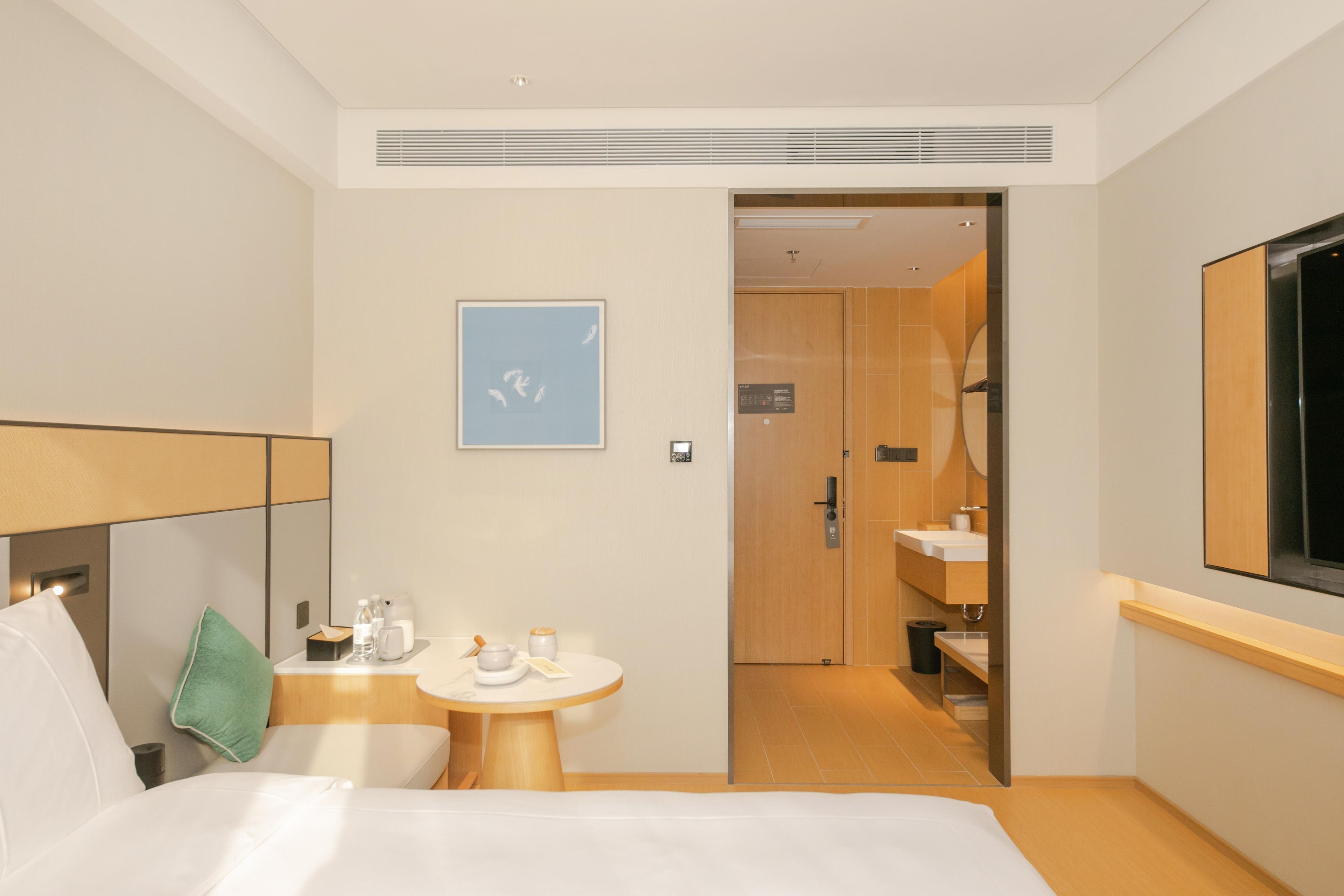 Ett hotellrum med en säng, ett litet bord med diverse bekvämligheter, en tavla och ett badrum som syns genom en öppen dörr.