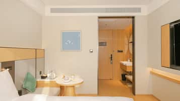 A hotel room with a bed, a small table with amenities, a painting, and a bathroom visible through an open door.