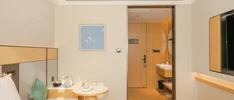 A hotel room with a bed, a small table with amenities, a painting, and a bathroom visible through an open door.
