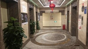 A hotel corridor with marble floors, potted plants, a red hanging ornament, and directional signs. - Qinghai Hotel (Shenzhen)