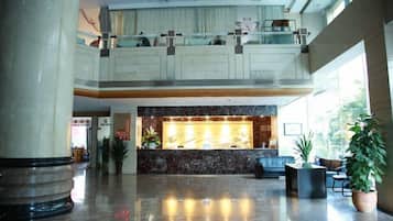 Un vestíbulo de hotel con mostrador de recepción, zona de estar y un balcón en el segundo piso.