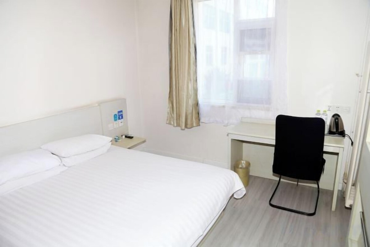 A hotel room with a bed, a desk, a chair, and a window with curtains.