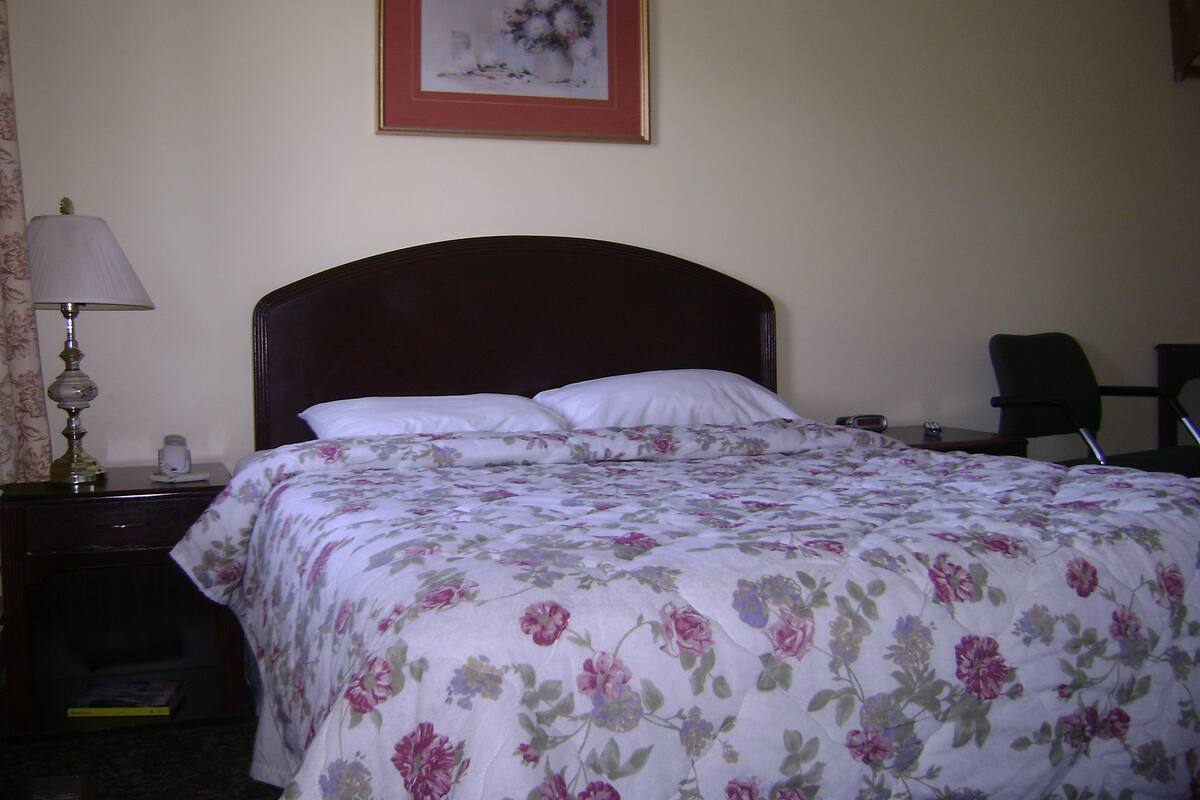 A neatly made bed with a floral bedspread, a bedside lamp, and a framed picture on the wall.