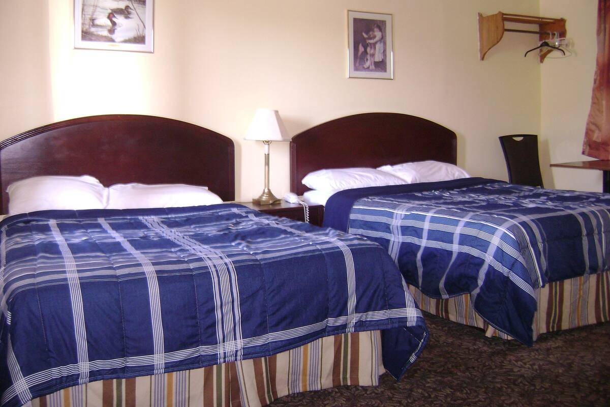 A hotel room with two beds, each with a blue and white striped bedspread, a wooden headboard, a bedside lamp, and a framed picture on the wall.