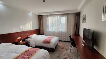 A hotel room with two beds, a desk, a television, and a window with curtains.