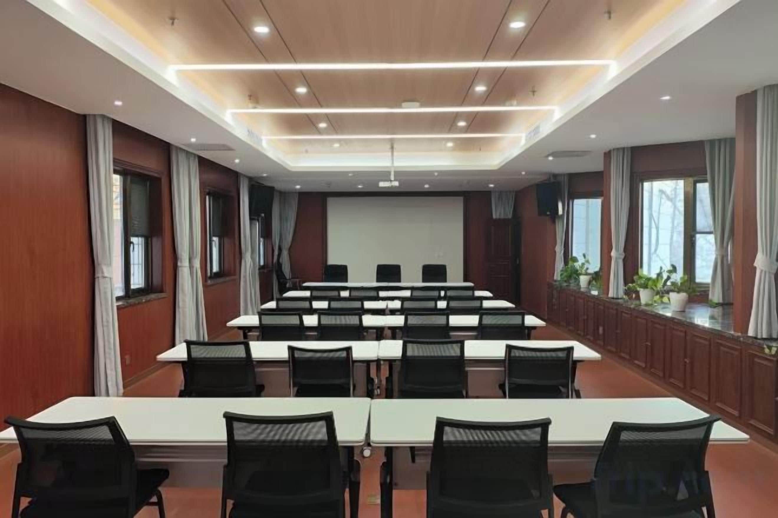 Un salón de conferencias con una larga mesa, sillas, una pantalla de proyector y un ventanal amplio.