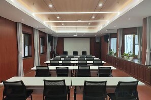 Un salón de conferencias con una larga mesa, sillas, una pantalla de proyector y un ventanal amplio.