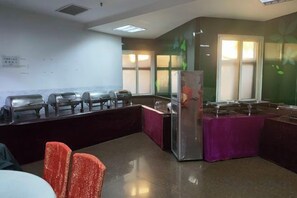 Ein Konferenzraum mit langem Tisch, Stühlen, einem Kühlschrank und einem Fenster mit Jalousien.