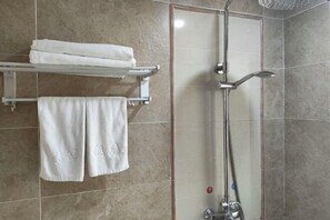 Un bagno con doccia vetrata, un portasciugamani con asciugamani piegati e una parete rivestita in piastrelle.