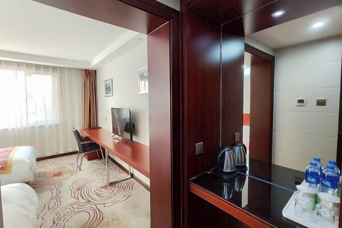 Una camera d'hotel con un letto, una scrivania, una sedia, una televisione, una macchina del caffè e un vassoio con bottiglie d'acqua.