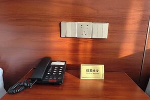 Una scrivania in legno con un telefono, una presa di corrente e una targhetta.