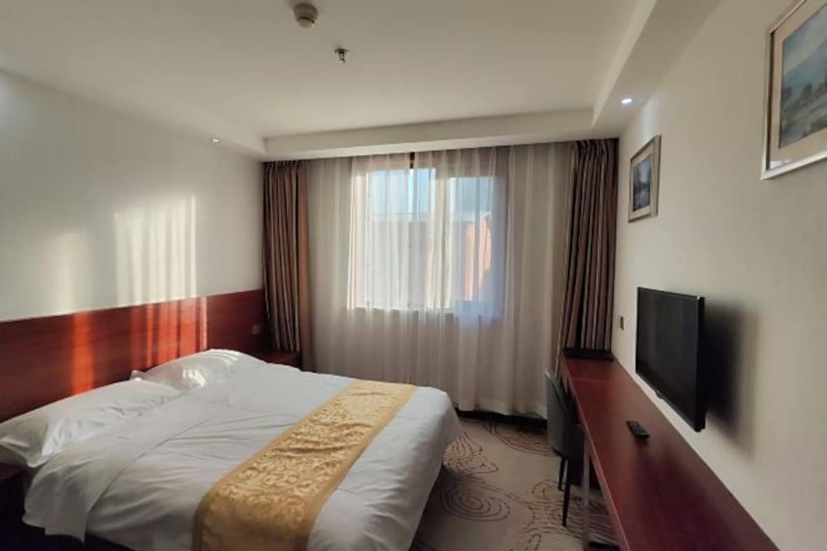 A hotel room with a bed, a TV, a desk, and a window with curtains.