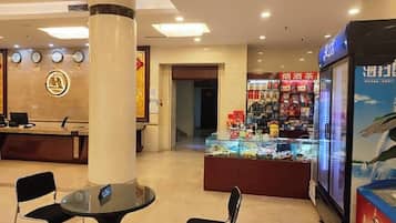 A hotel lobby with a reception desk, a glass display case with snacks, and a seating area with chairs.