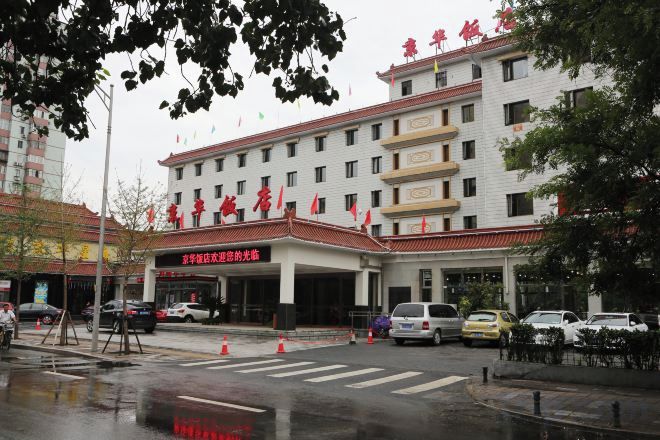 A multi-story hotel with a red and white facade, a covered entrance, and a parking area with cars.