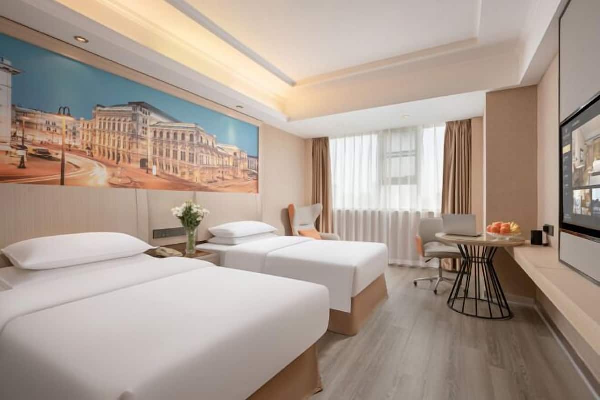 A hotel room with two beds, a desk, a chair, a TV, and a painting on the wall.