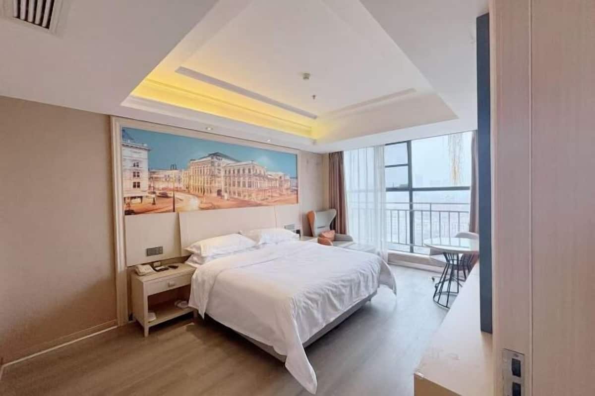 A hotel room with a large bed, a nightstand, a desk, a chair, and a window with a view.