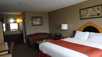 Habitación de hotel con cama, escritorio, silla, mesita de noche, lámpara y espejo.