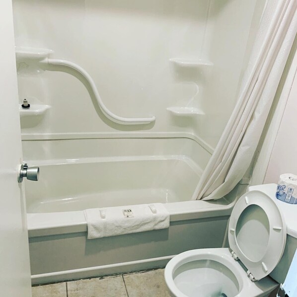 A bathroom with a bathtub, toilet, and shower curtain. - Atlanta Motel (Orangeville)