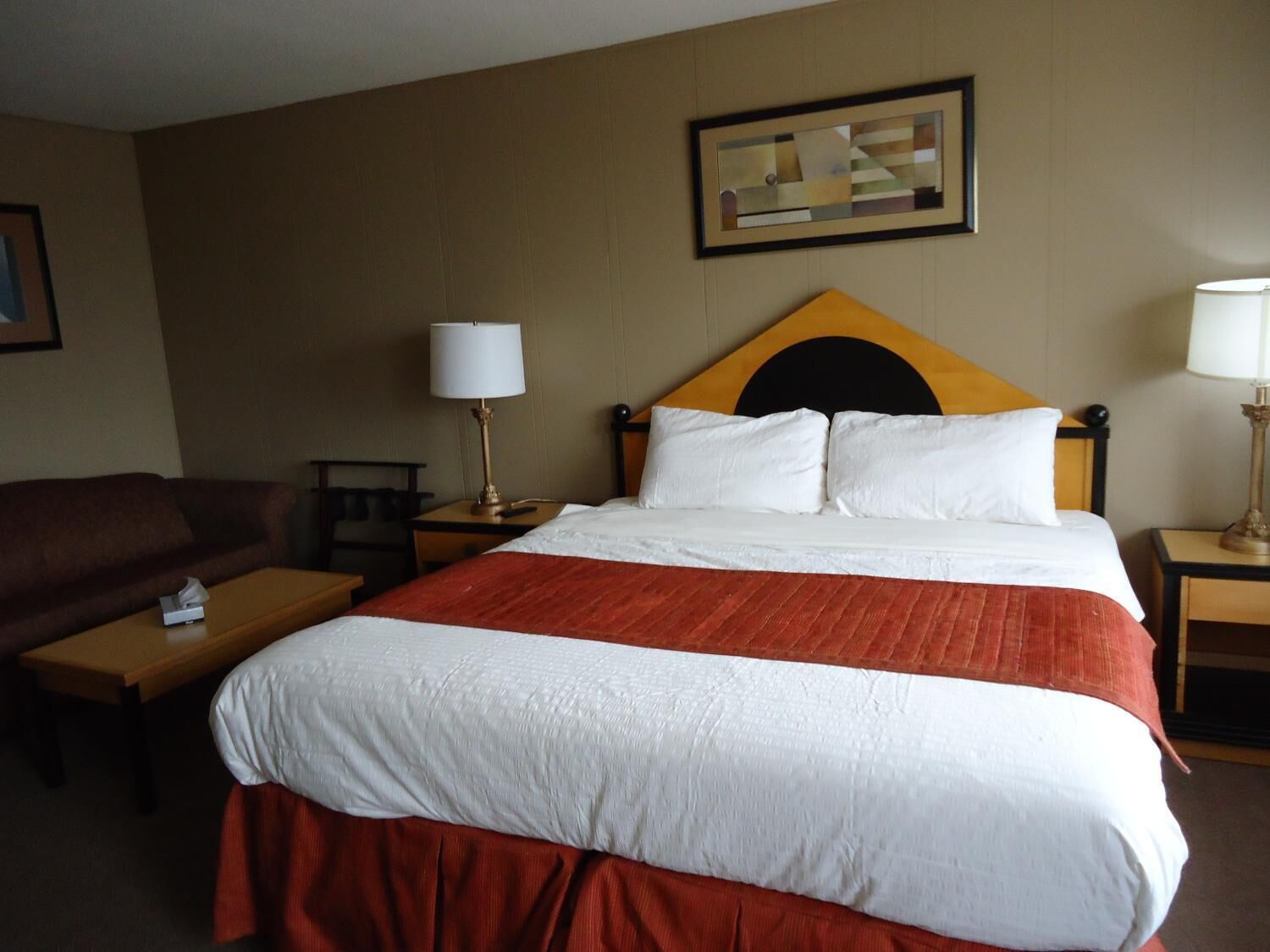 A hotel room with a bed, two bedside tables, a nightstand, a lamp, a couch, and a framed picture on the wall.