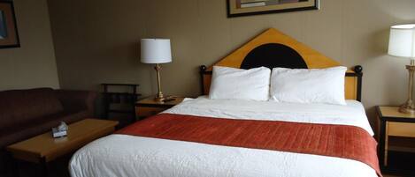 A hotel room with a bed, two bedside tables, a nightstand, a lamp, a couch, and a framed picture on the wall.