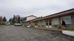 Un motel con una hilera de habitaciones, un estacionamiento y una persona caminando cerca del edificio.
