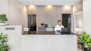 A reception desk with a sign labeled "RECEPTION," a receptionist, and a potted plant to the left. - Chaweng terrace (Koh Samui)