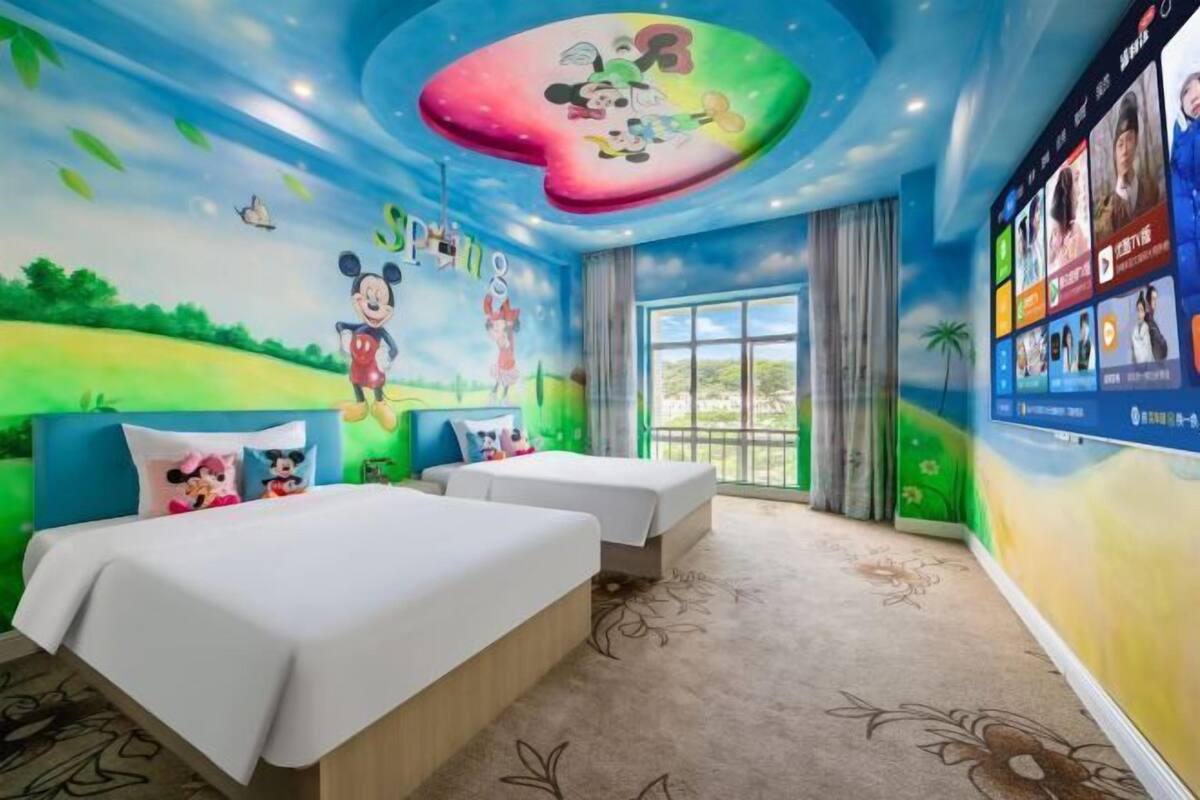 Ein Kinderzimmer mit Wandgemälden von Mickey Mouse und Minnie Mouse, zwei Betten und einem großen Fenster.