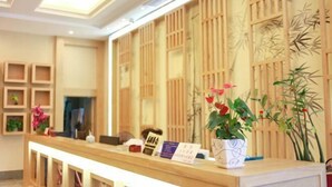 A reception desk with a wooden panel backdrop, a white vase with flowers, and a few informational cards. - Xi Yue Hotel（Guangzhou Changlong Nancun area） (Guangzhou)