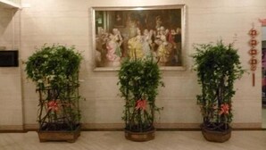 A reception area with a framed painting on the wall and three potted plants with red ribbons. - Hotspring Quanshangquan Hotel (Xianning)