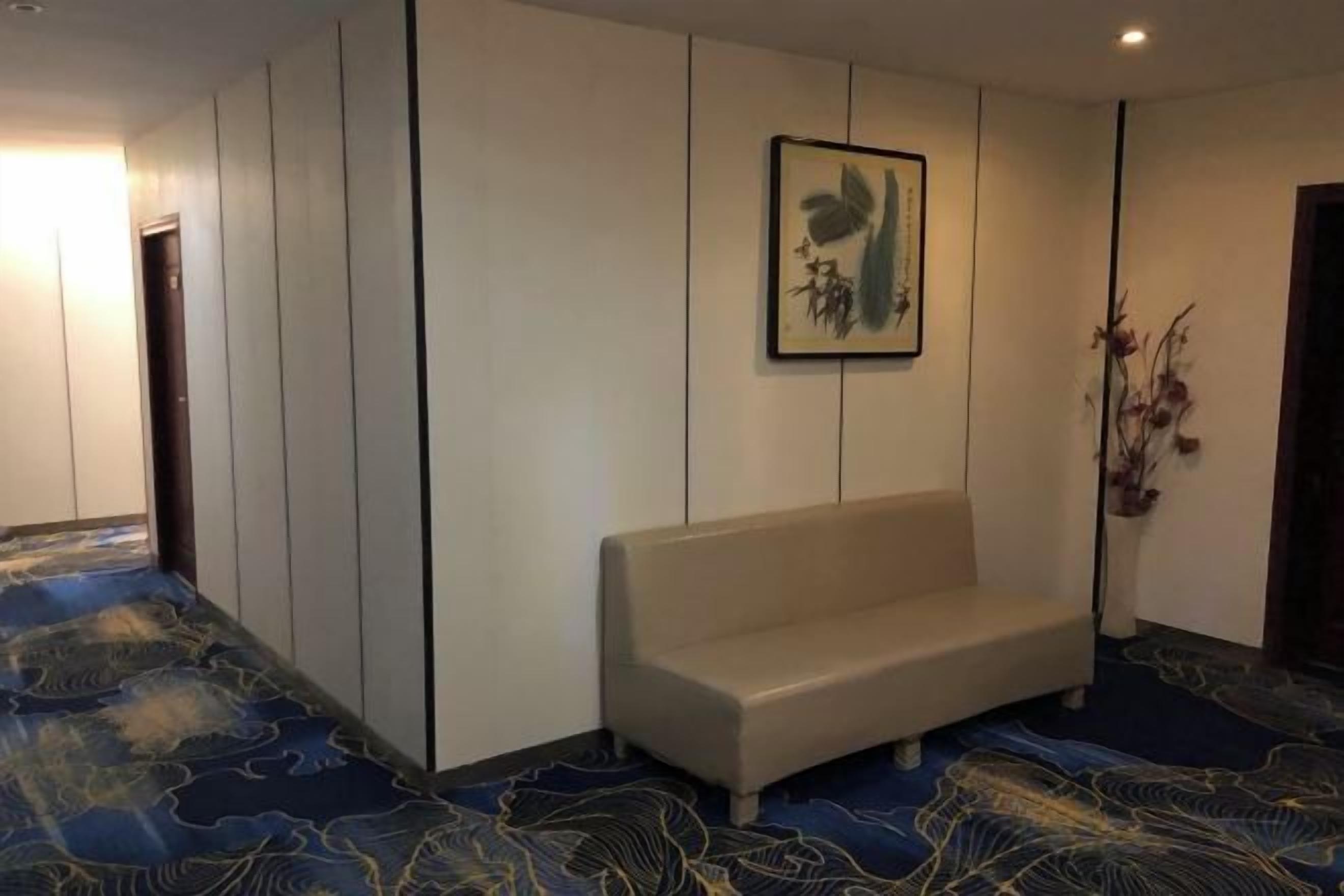 A room with a bench, a framed artwork on the wall, and a patterned carpet.
