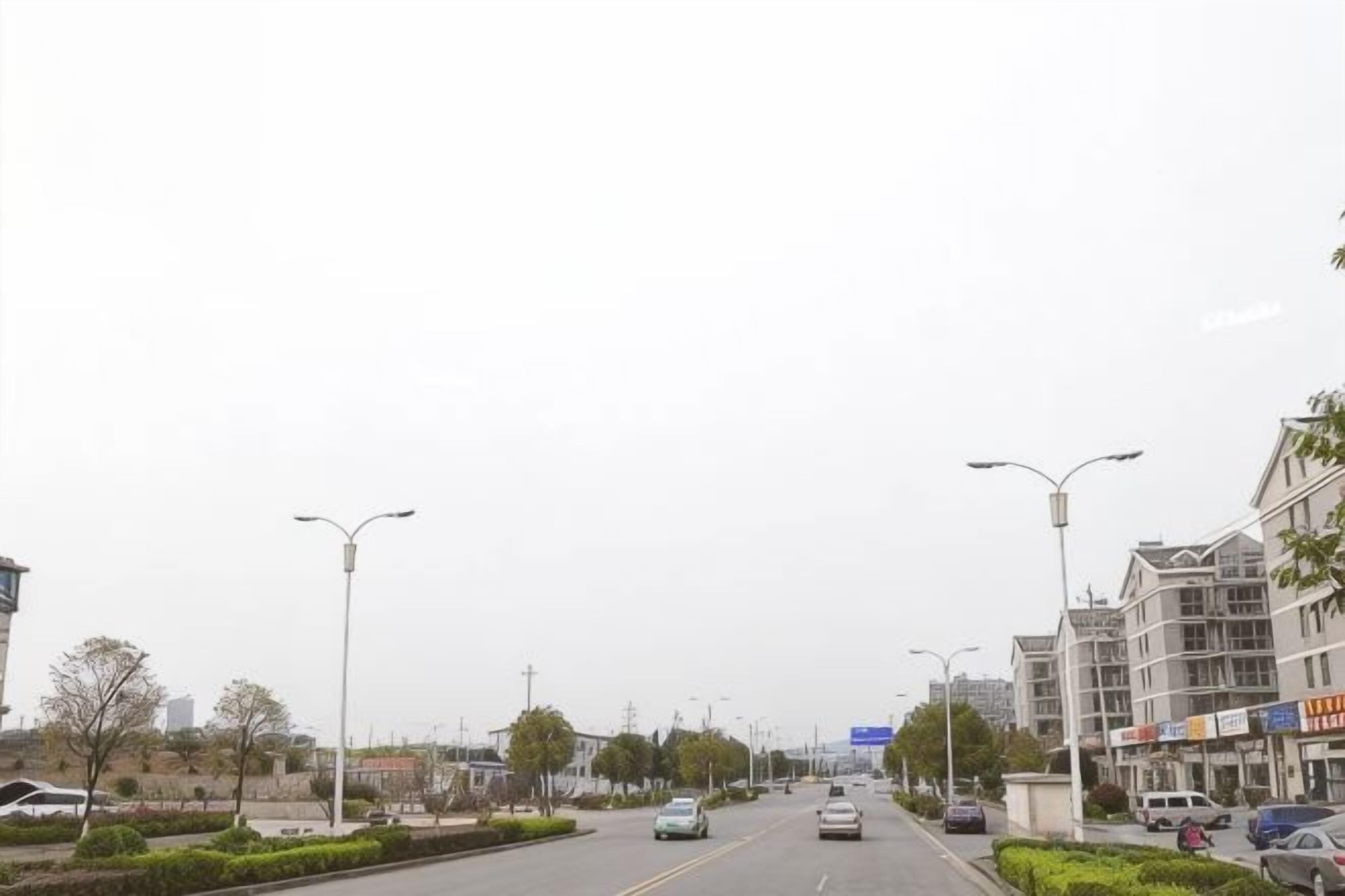 A wide urban road with multiple lanes, streetlights, and buildings on both sides.