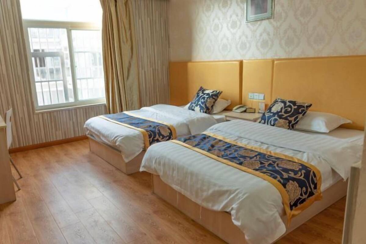 A hotel room with two beds, a window with curtains, a patterned wall, and a wooden floor.