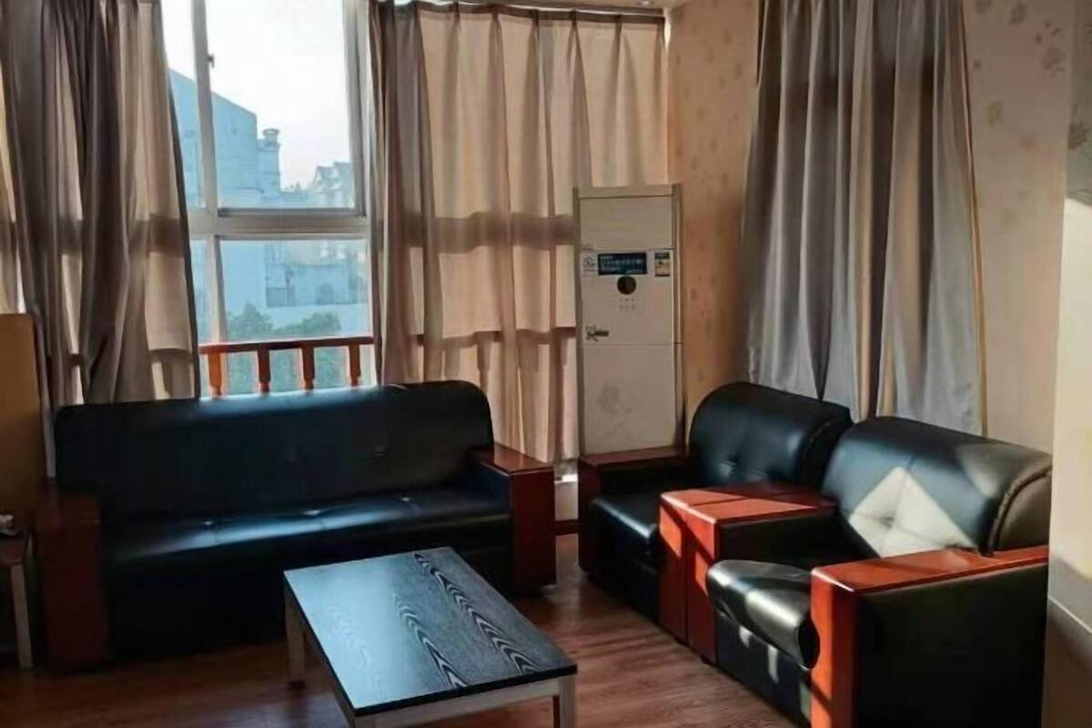 A room with a sofa, a smaller couch, a table, and a window with curtains.