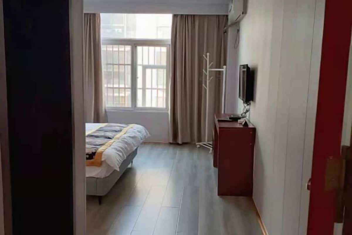 A hotel room with a bed, a TV, a desk, and a window with curtains.