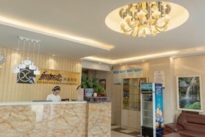 Ein Hotel-Empfangsbereich mit Marmor-Theke, einer Rezeptionistin, einer Kandelaber, einem Empfangstresen, einer Sitzecke und einer Wanduhr.