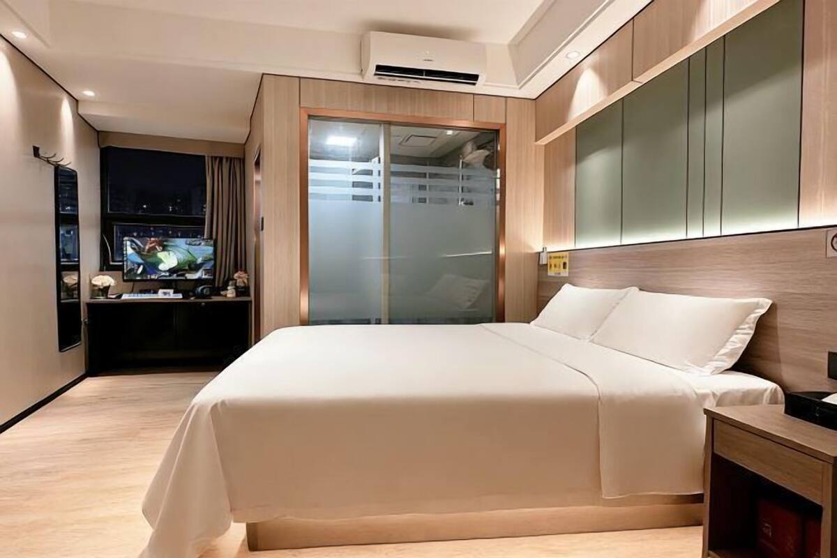 A modern hotel room with a large bed, a TV, a wardrobe, and a view of the city at night.